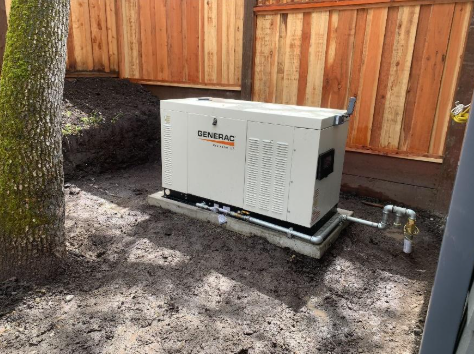 A generator is sitting in the dirt in front of a wooden fence.