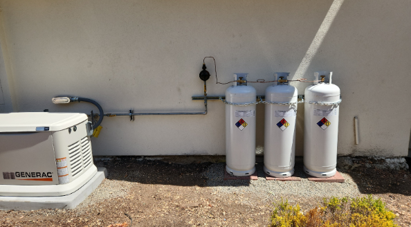 Three gas tanks are sitting next to a generator on the side of a building.