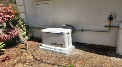 A white generator is sitting outside of a house.