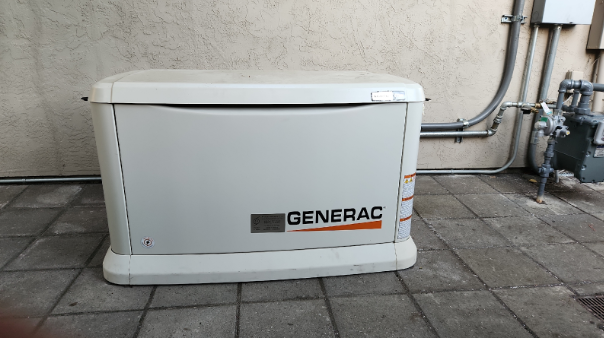 A generator is sitting on the sidewalk next to a wall.