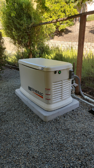 A generator is sitting on top of a gravel covered ground next to a fence.
