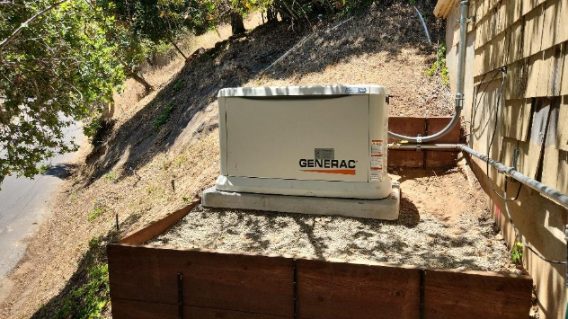 A generator is sitting on top of a wooden box on the side of a house.