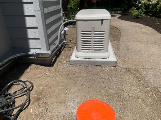 A generator is sitting on the side of a house next to a bucket.