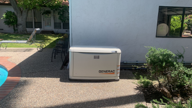 A generator is sitting on the side of a house.