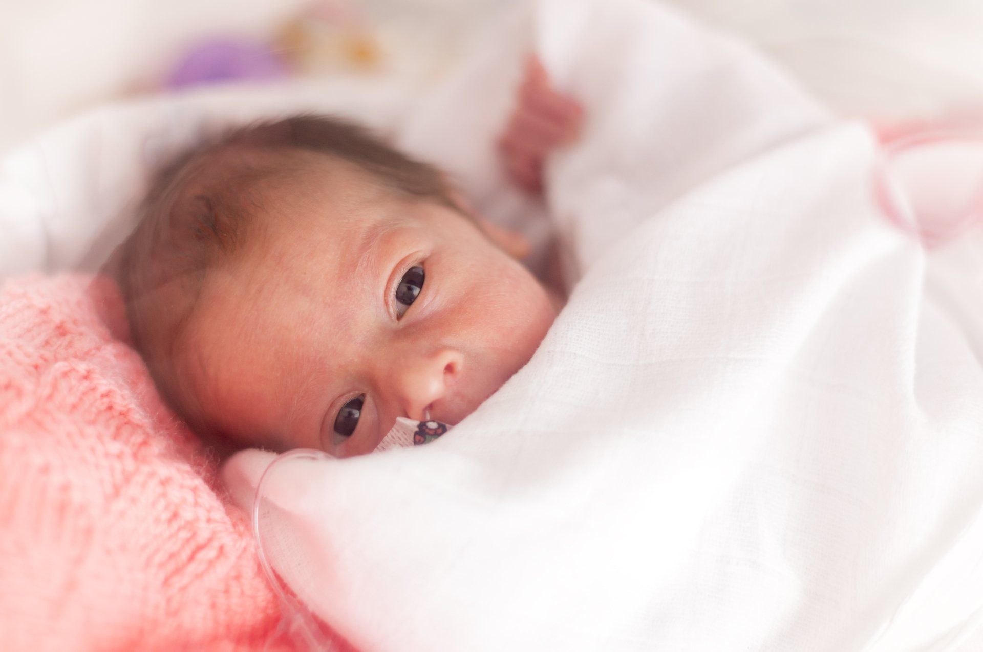 A newborn baby is wrapped in a pink blanket and looking at the camera.