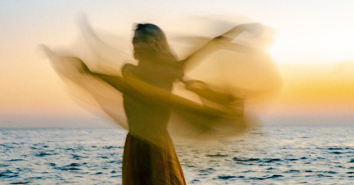 A woman is holding a scarf in the wind at sunset.