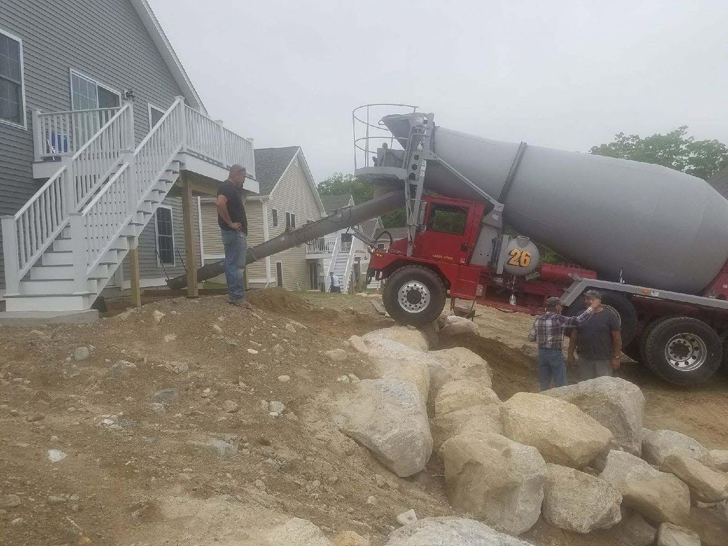 Concrete mixer truck pouring cement beside an apartment building, with workers and a staircase in view