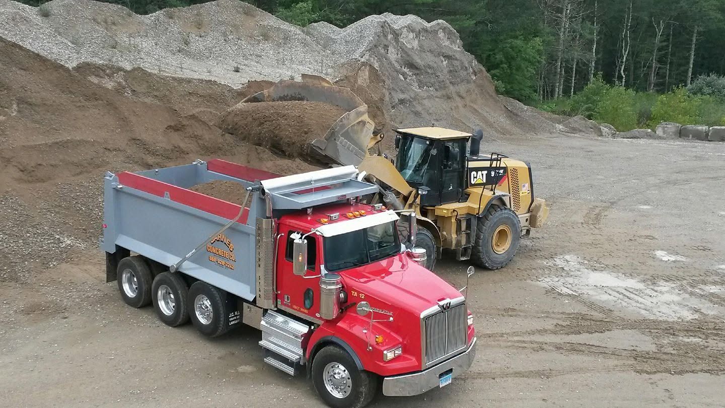 Red dump truck and yellow loader at a gravel quarry, with the truck bed partly filled.