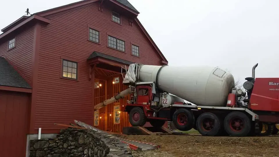 Red barn with a red-and-gray cement mixer truck pouring into an upper doorway.