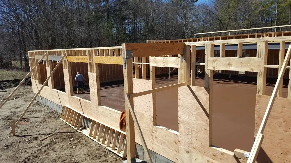 Wood-framed house under construction with workers and exposed walls in a sunny outdoor setting