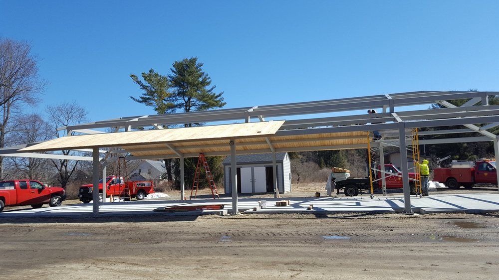 Partially built metal carport with several parked red vehicles on a sunny day