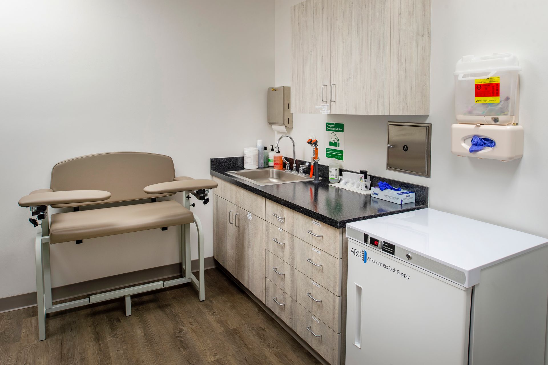 A doctor 's office with a table , sink , and refrigerator.