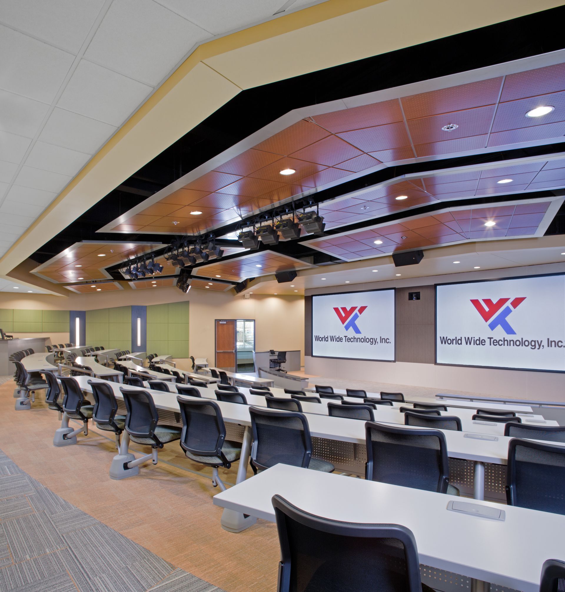 A large room with tables and chairs and a large screen that says x on it