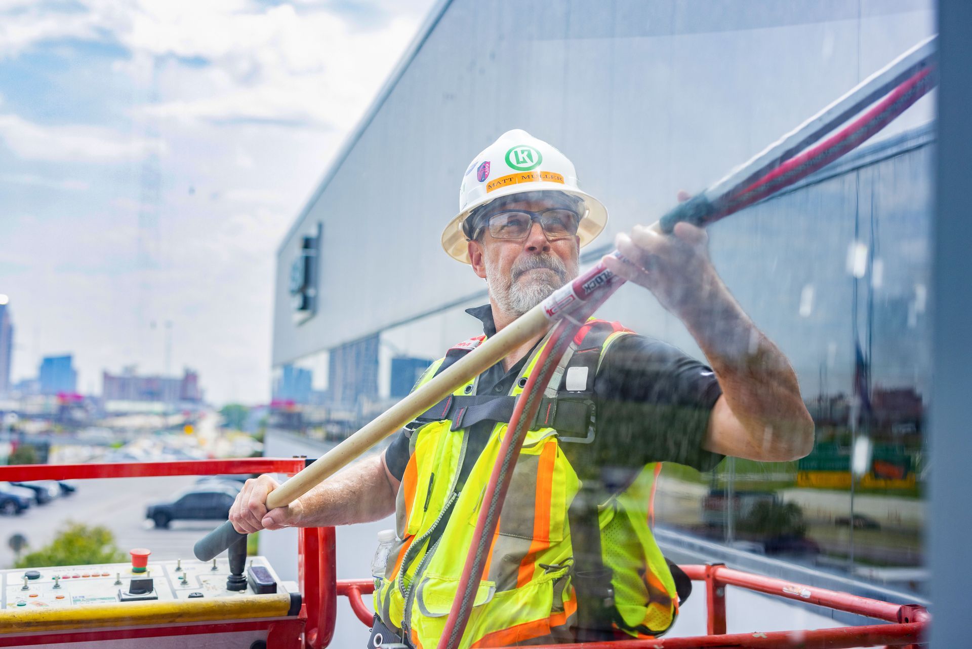 A construction worker is cleaning a building window with a broom.