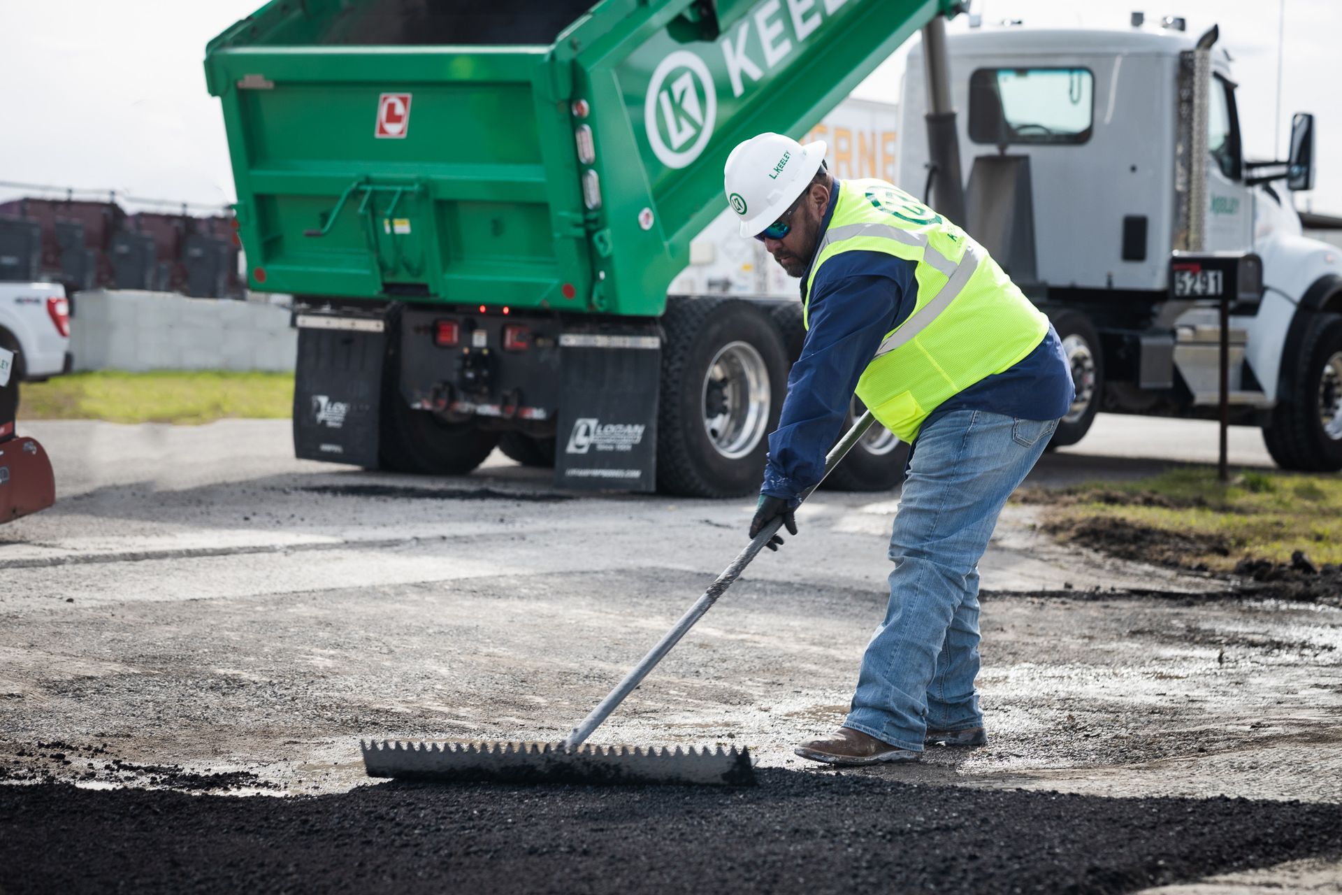 A man is sweeping the ground in front of a dump truck.