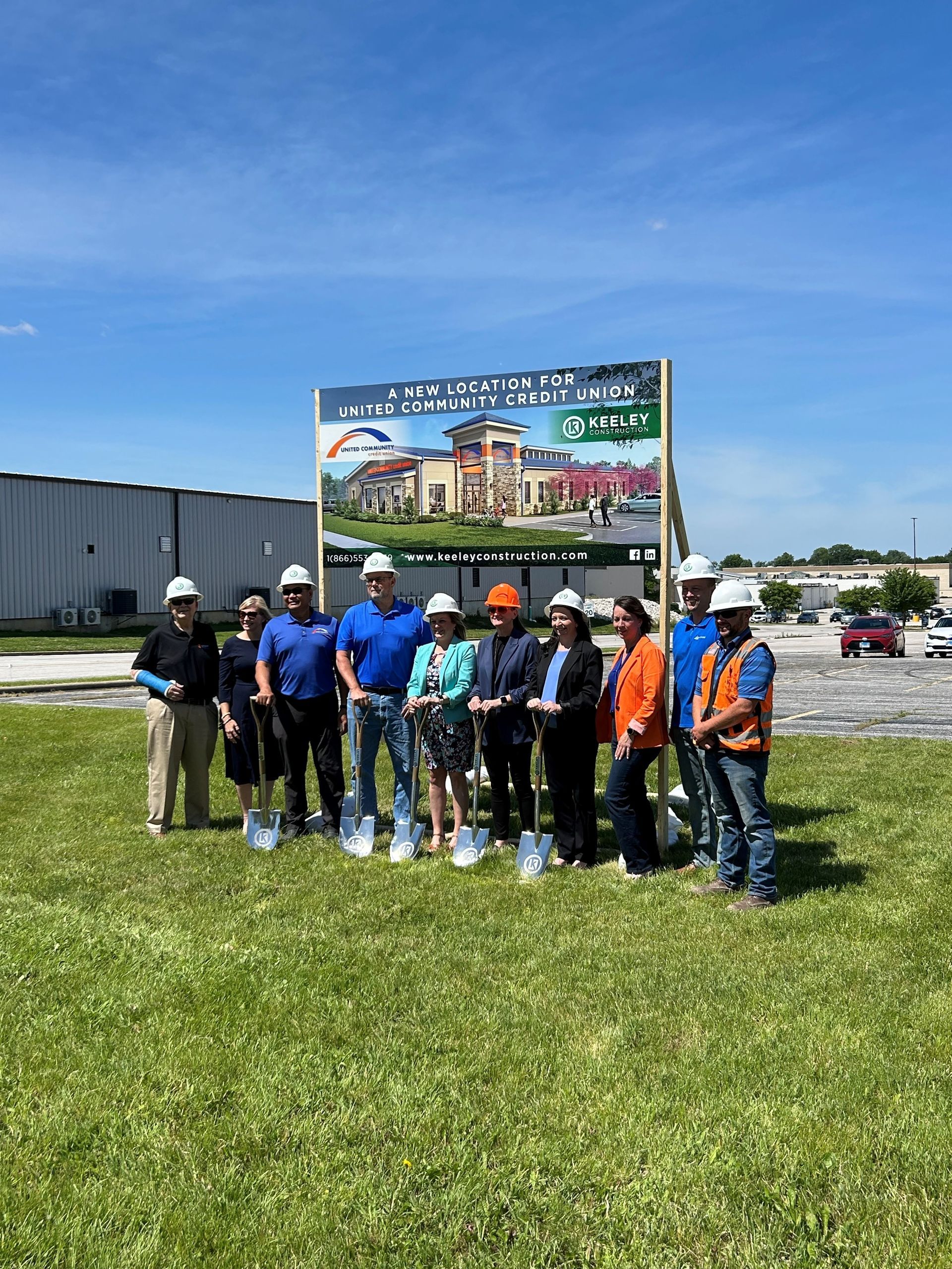 A group of people are standing in a field with shovels in front of a sign.
