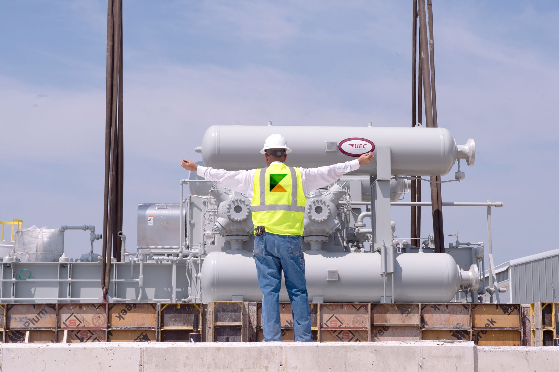 A man in a yellow vest and hard hat is standing in front of a large machine