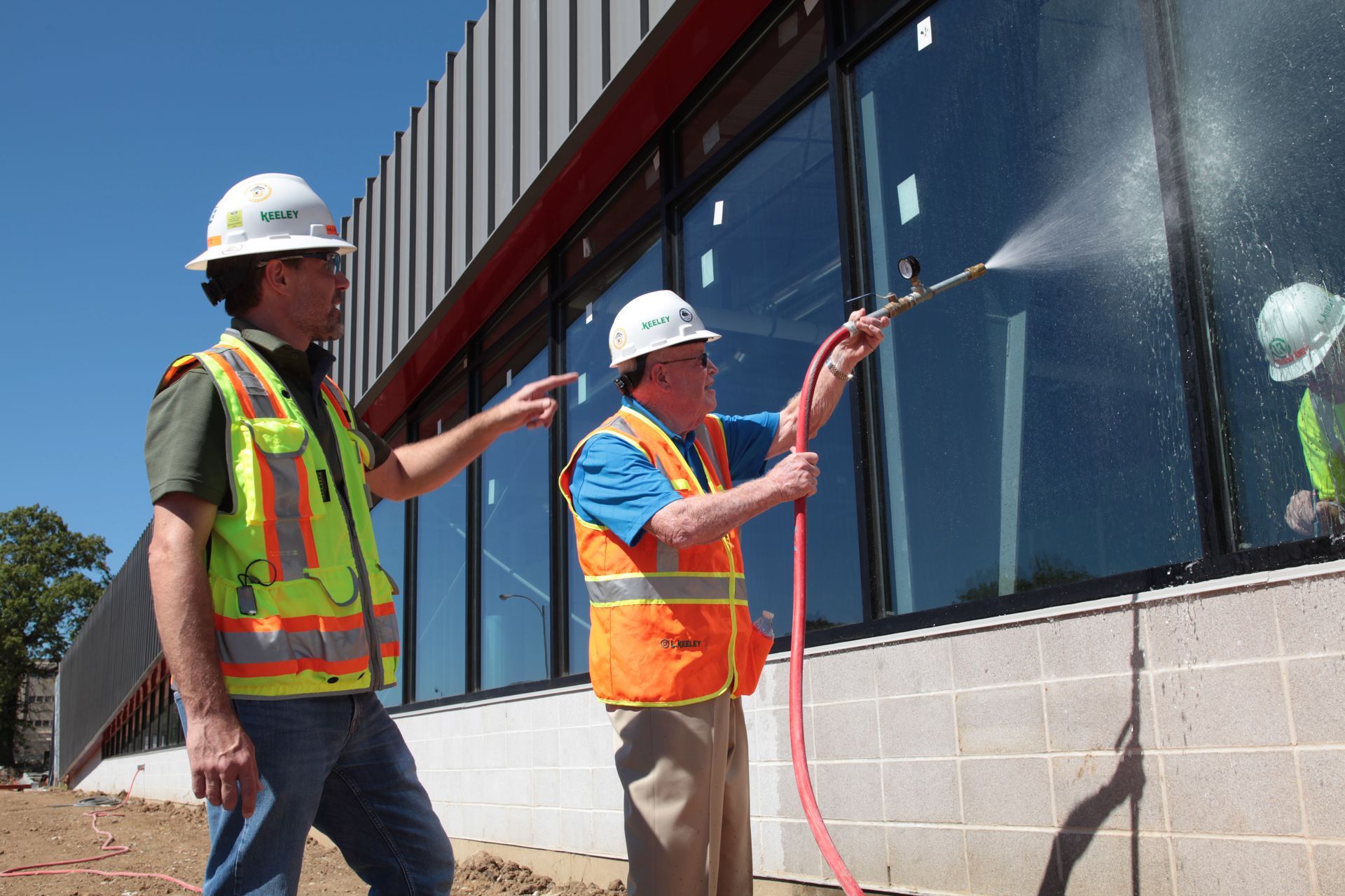 Two construction workers spraying a window with a hose