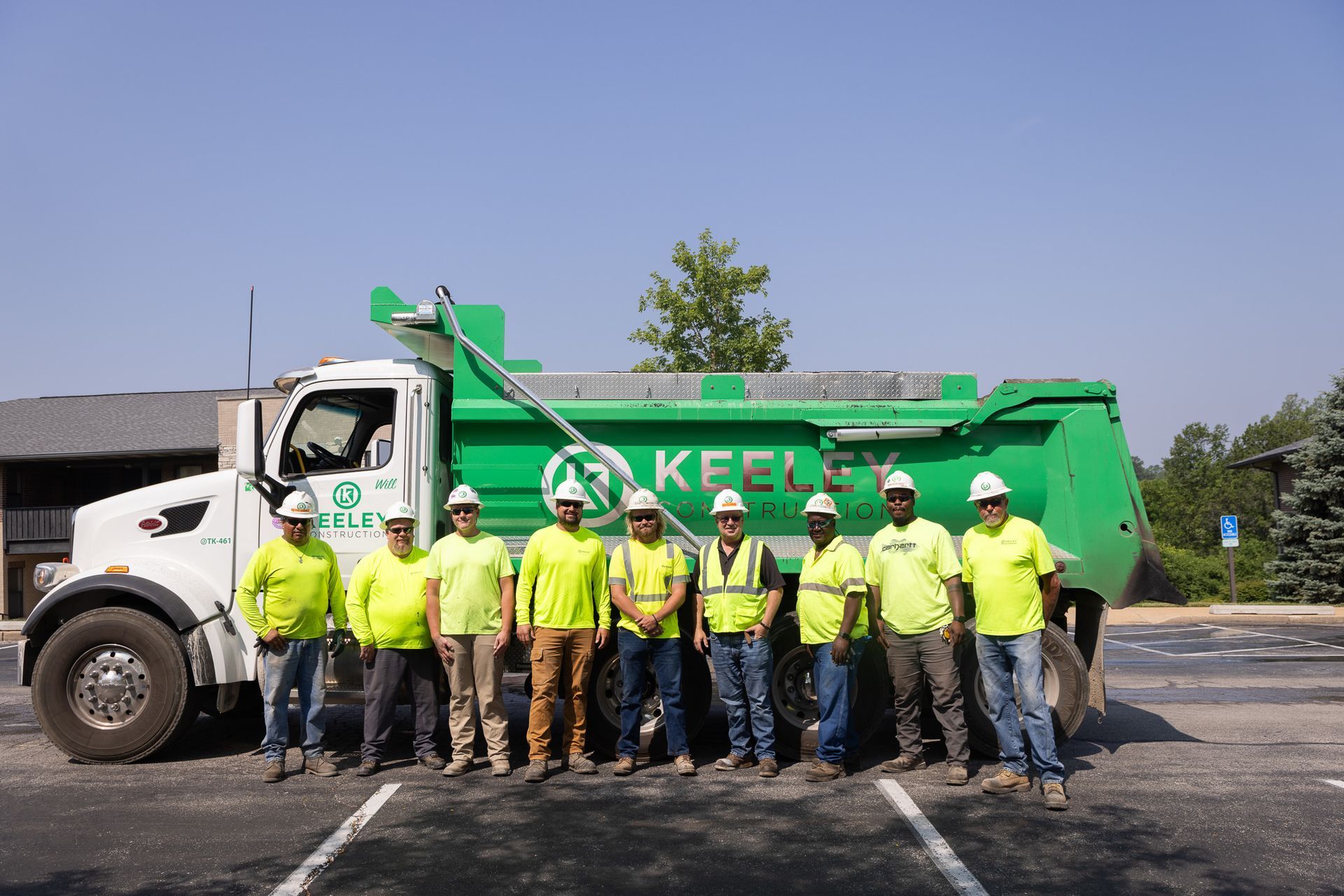 A group of construction workers are posing for a picture in front of a dump truck.