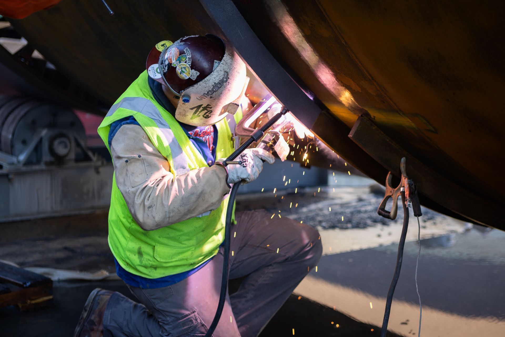 A man wearing a yellow vest and a helmet is welding a piece of metal.