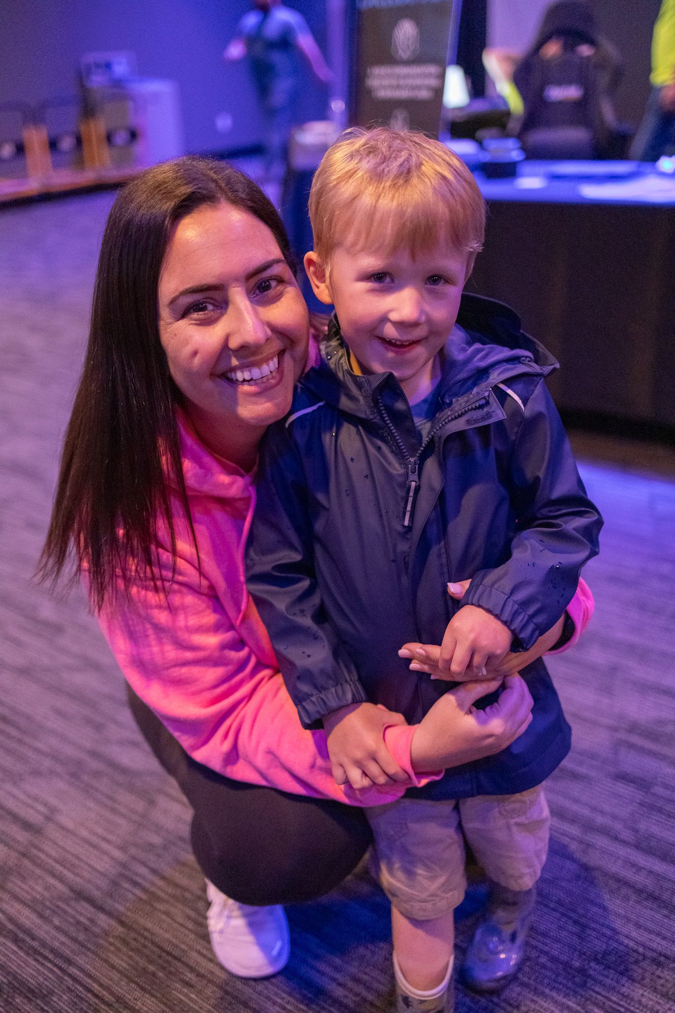 A woman is kneeling down next to a little boy in a blue jacket.