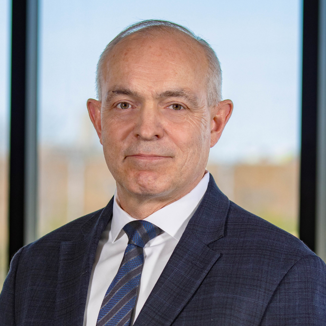A man in a suit and tie is standing in front of a window.