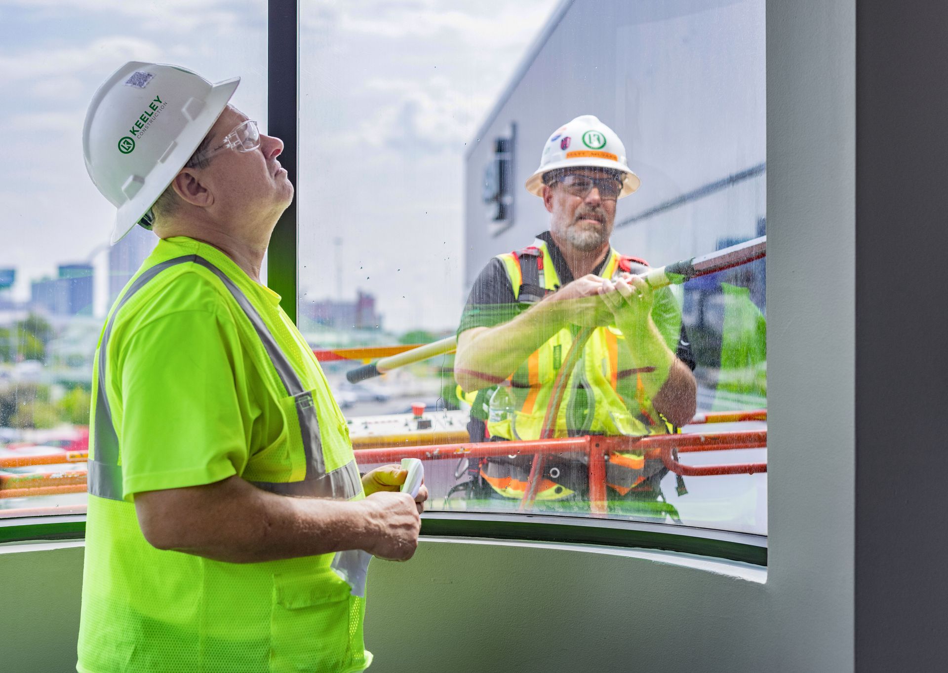 Two construction workers are standing next to each other in front of a window.