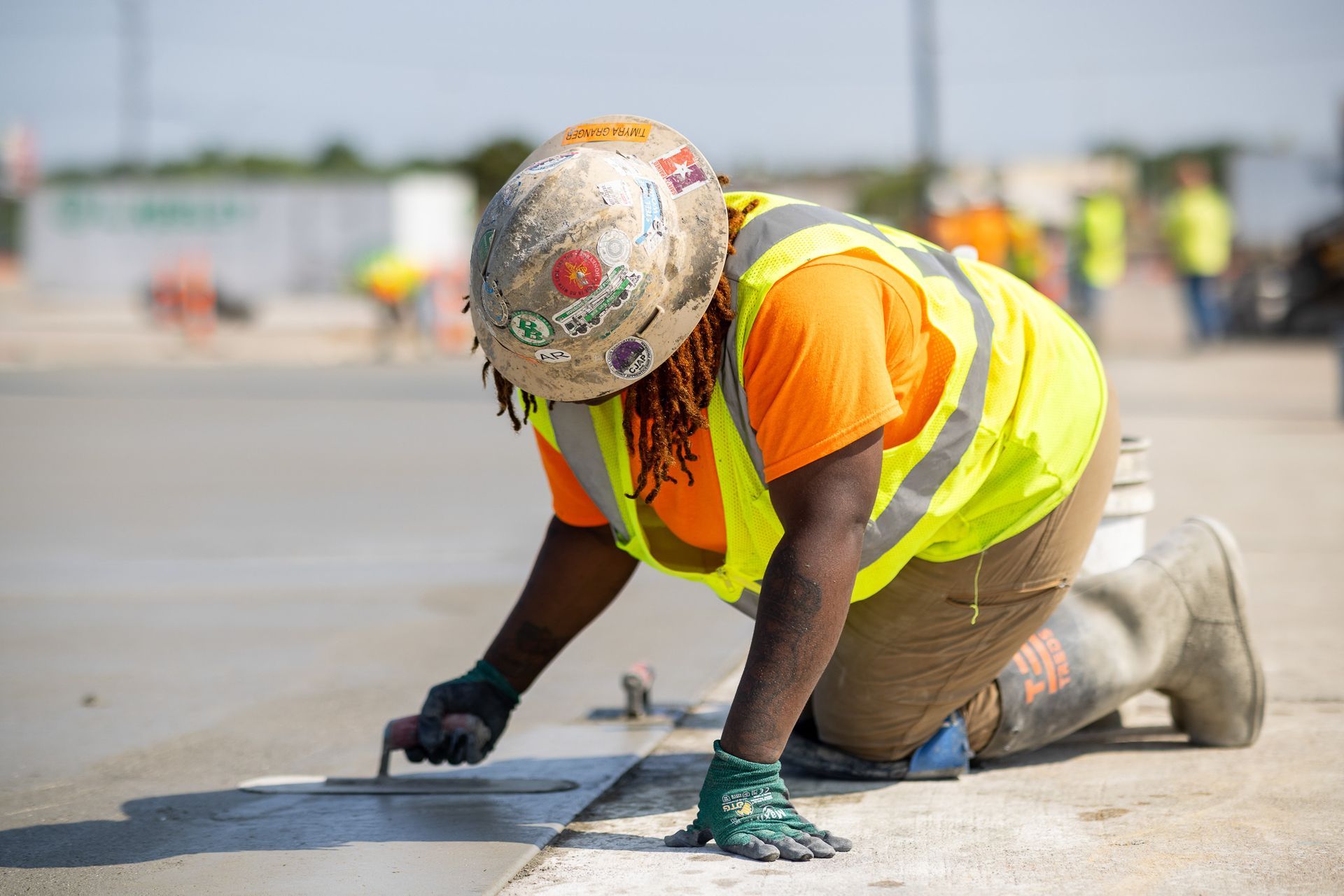 A construction worker is kneeling down and working on a concrete surface.