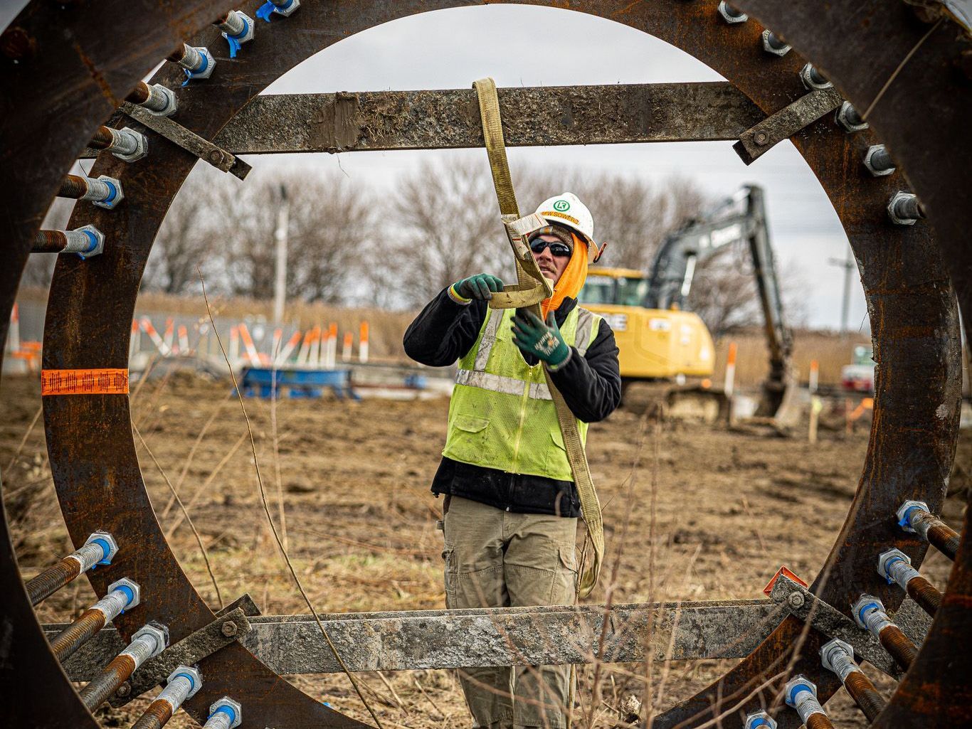 A construction worker is standing in front of a large metal ring.