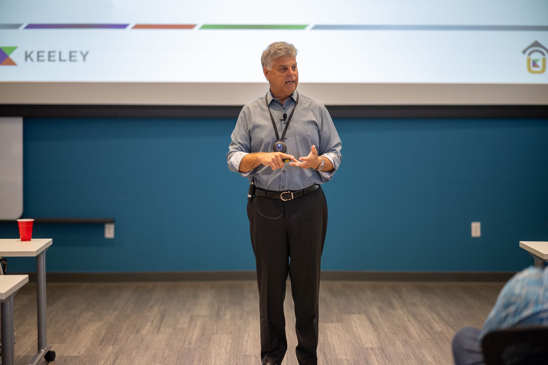 A man is giving a presentation in front of a blue wall.