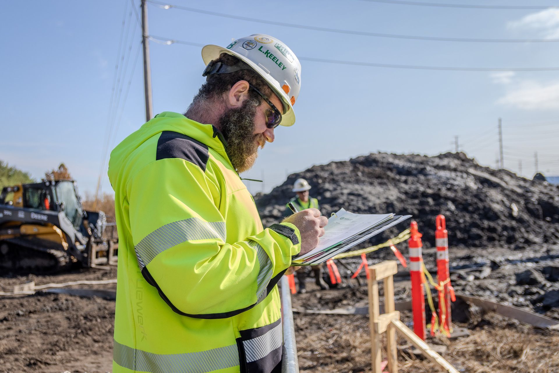 A construction worker is writing on a clipboard at a construction site.