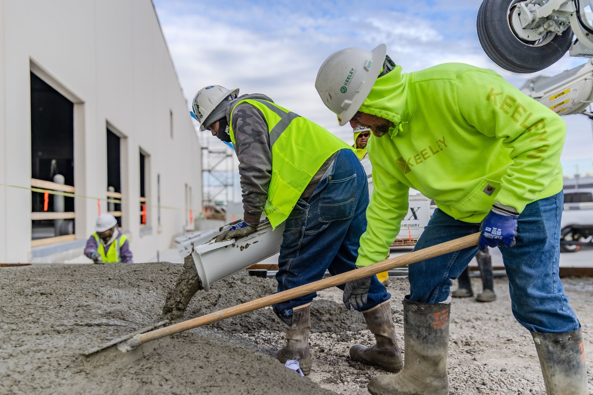 Two construction workers are pouring concrete on a construction site.