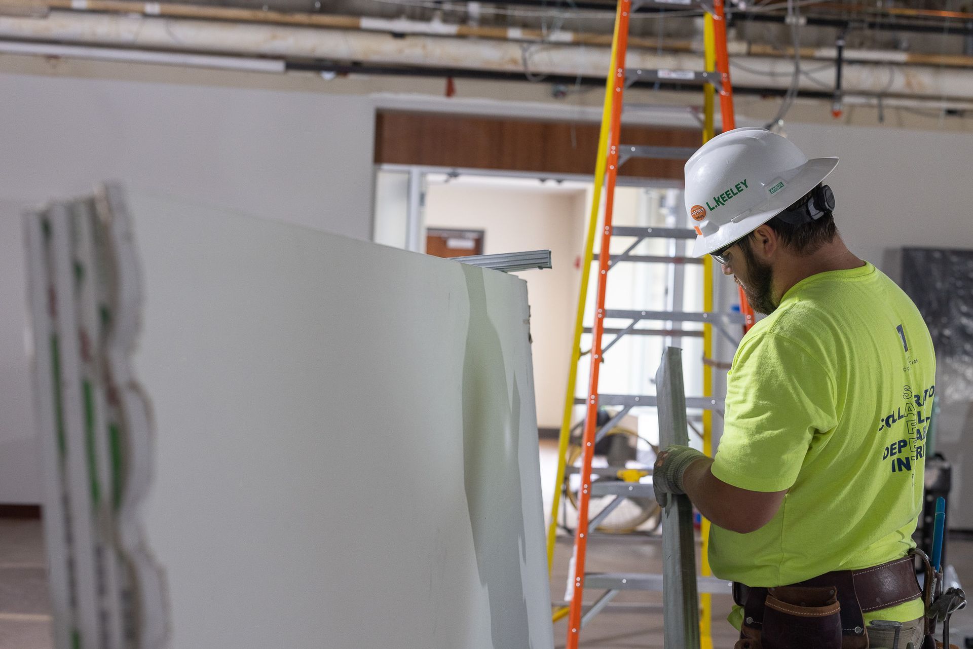 A man wearing a hard hat and safety vest is working on a wall.