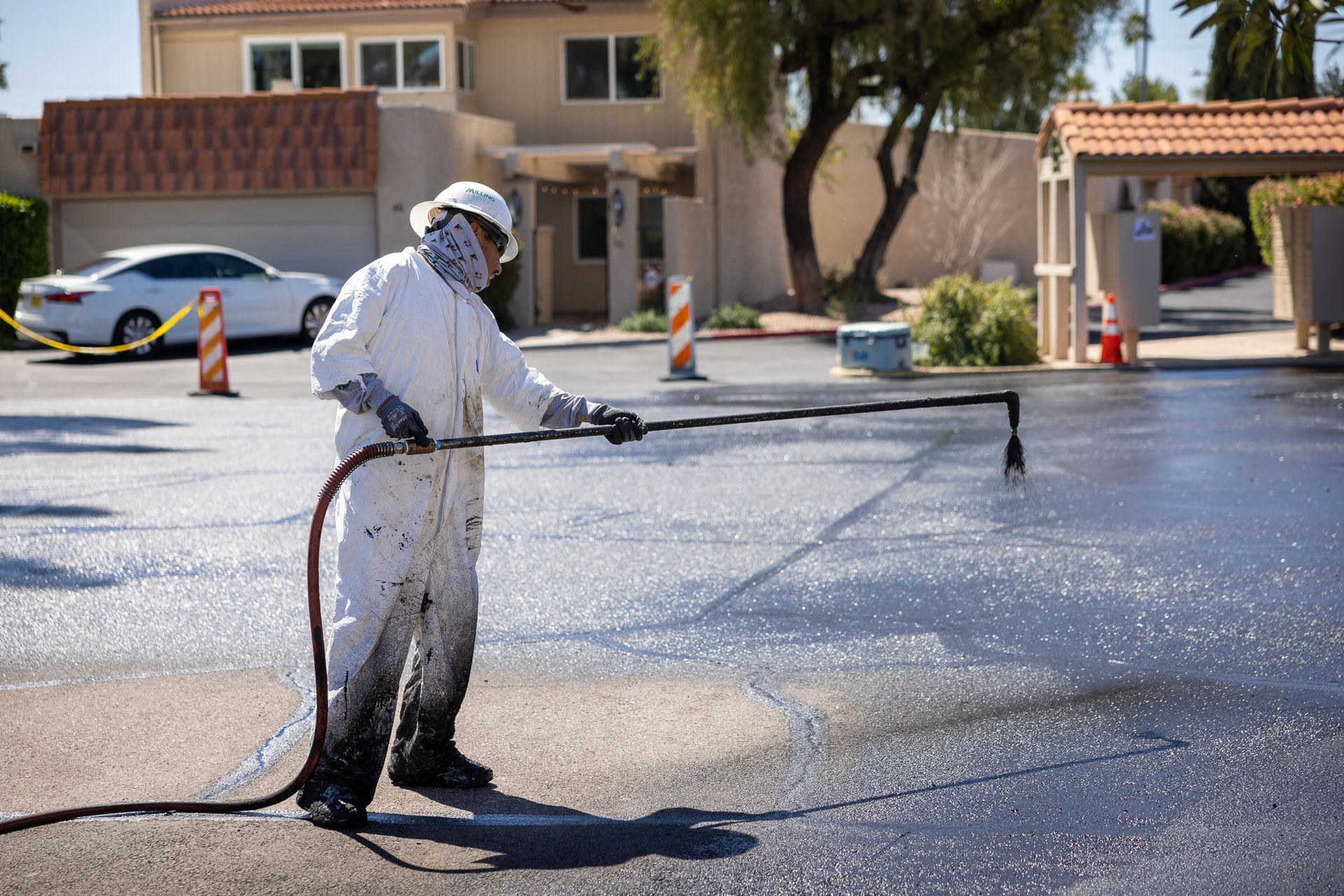 A man in a protective suit is spraying asphalt in a parking lot.