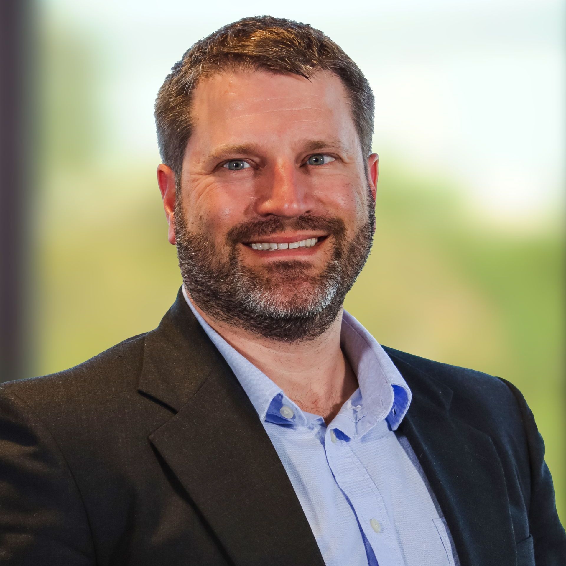 A man with a beard is wearing a suit and smiling for the camera.