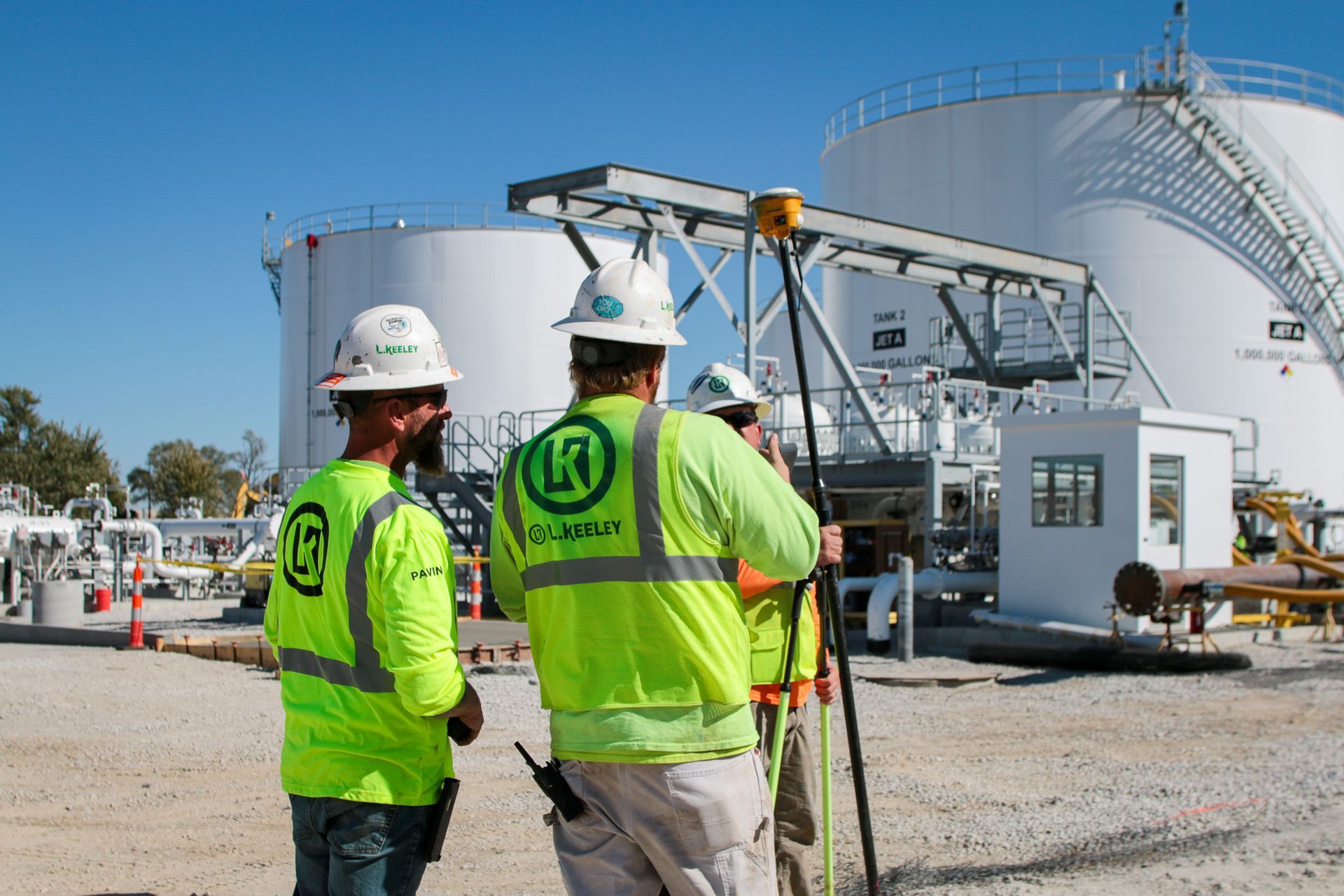 Two construction workers are standing in front of a large tank.