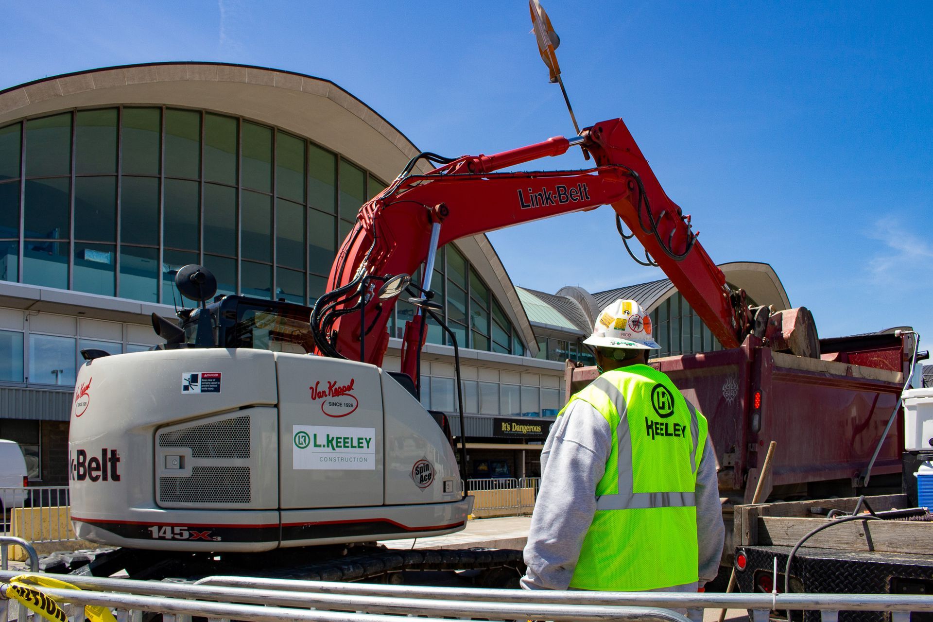 A man in a yellow vest is standing in front of an excavator.