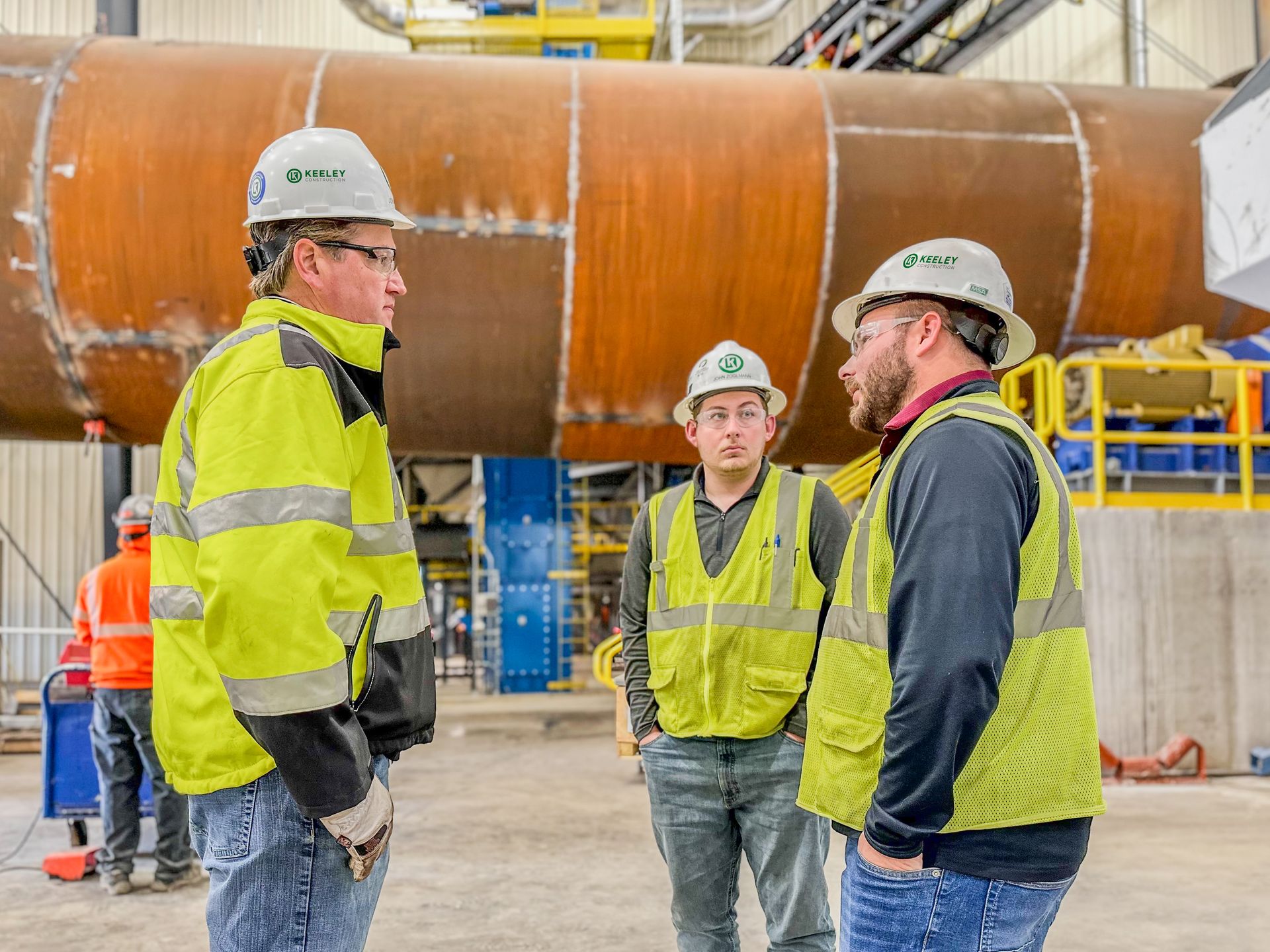 A group of construction workers are standing in a factory talking to each other.