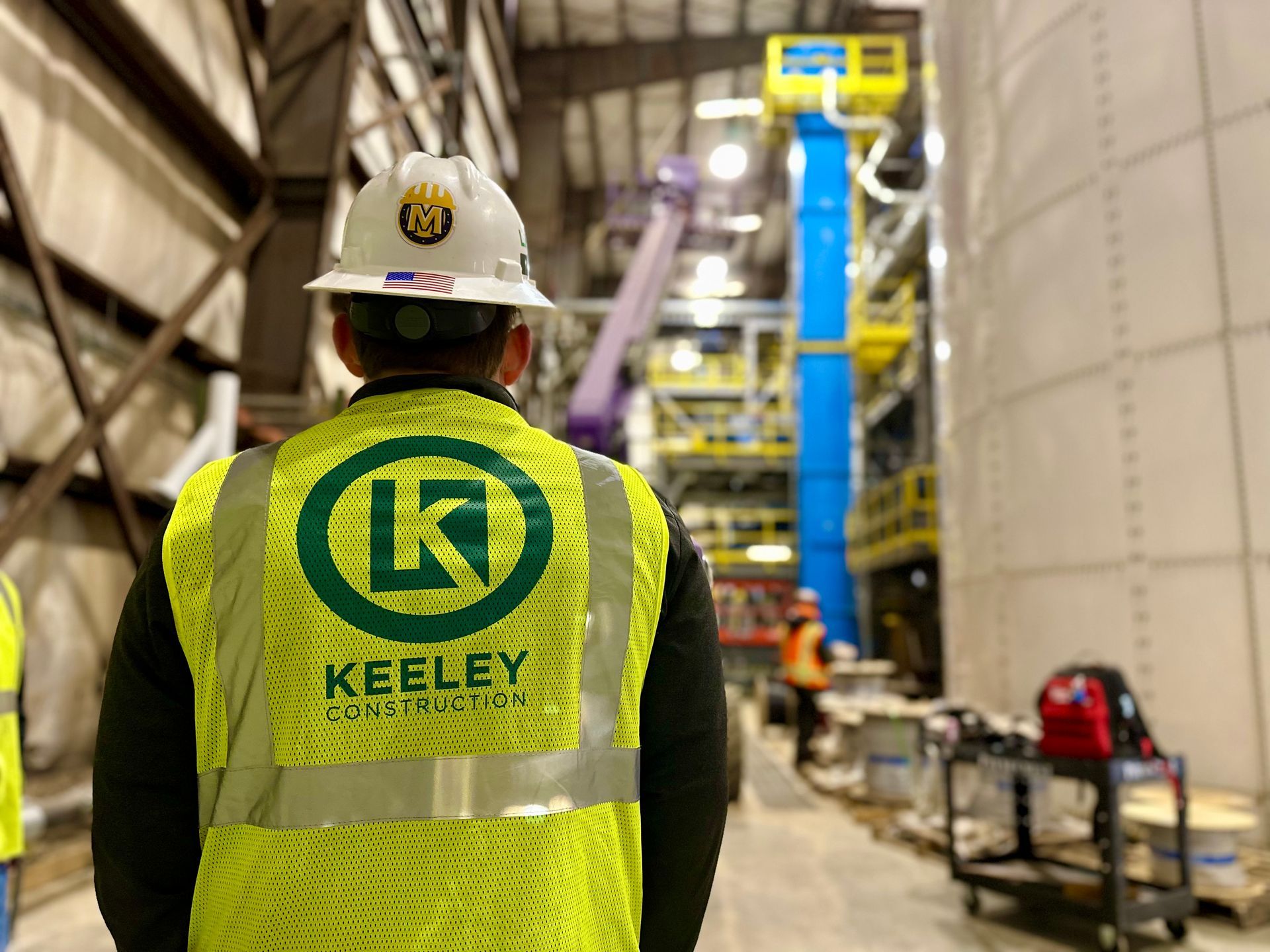 A man wearing a hard hat and a yellow vest is standing in a building.