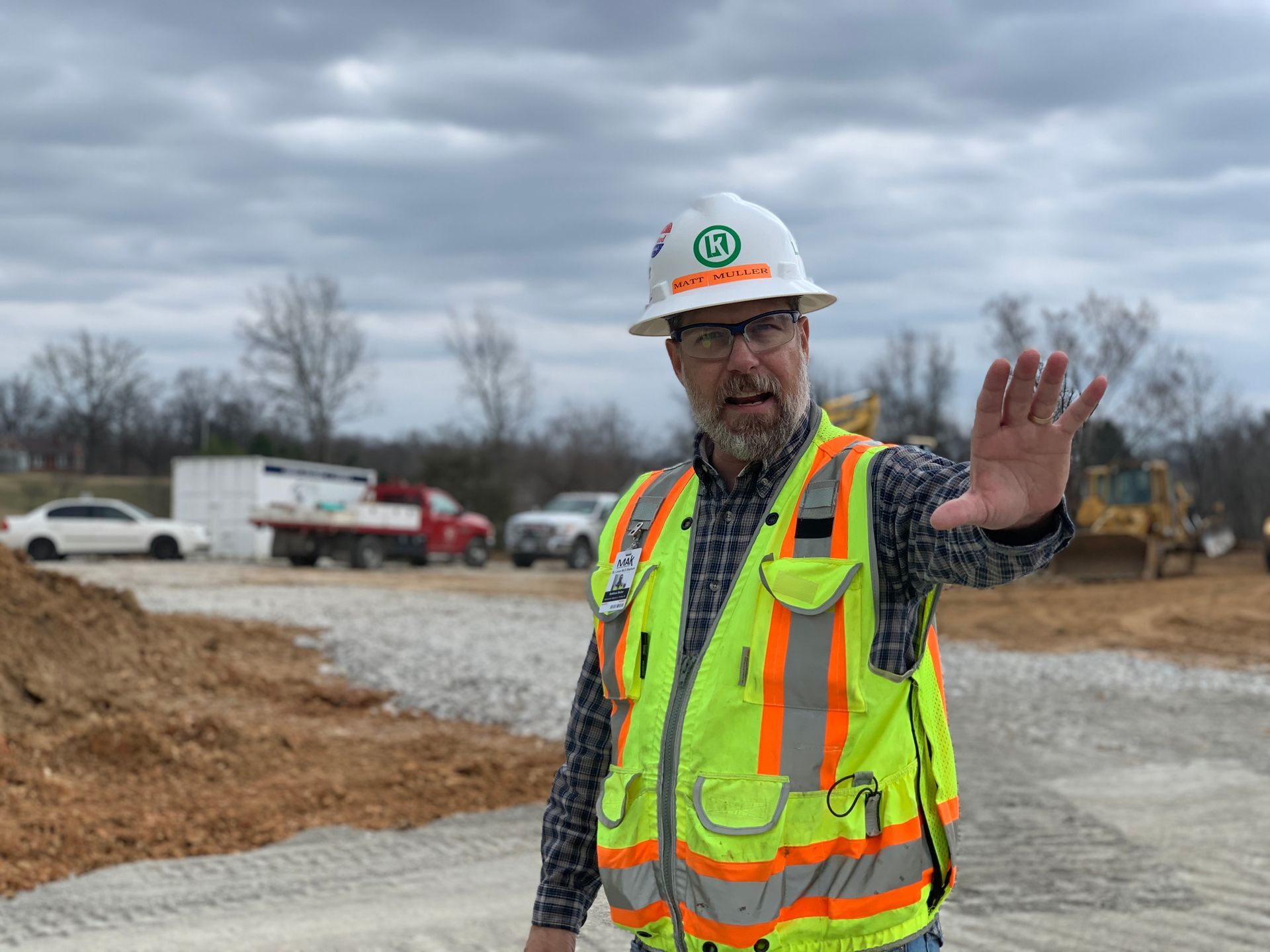 A man wearing a hard hat and safety vest is standing on a construction site.