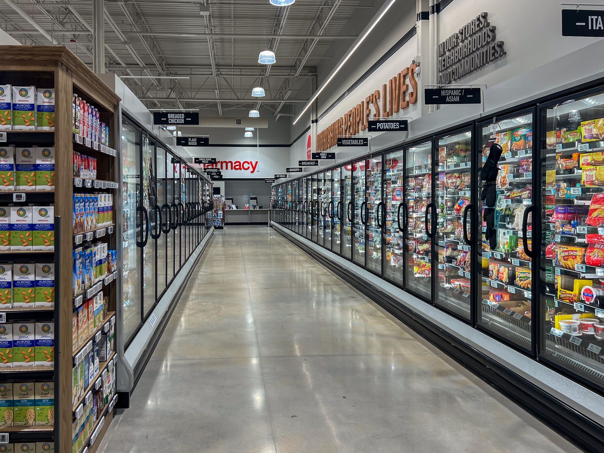 A long aisle of a grocery store with a pharmacy in the background.