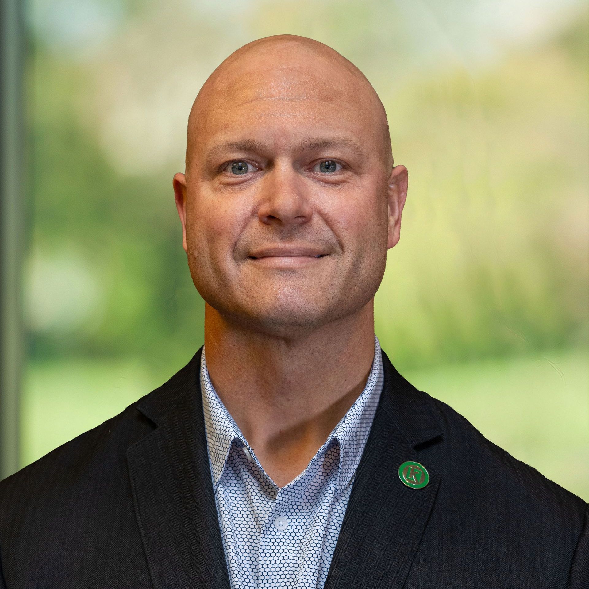 A bald man in a suit with a k pin on his jacket