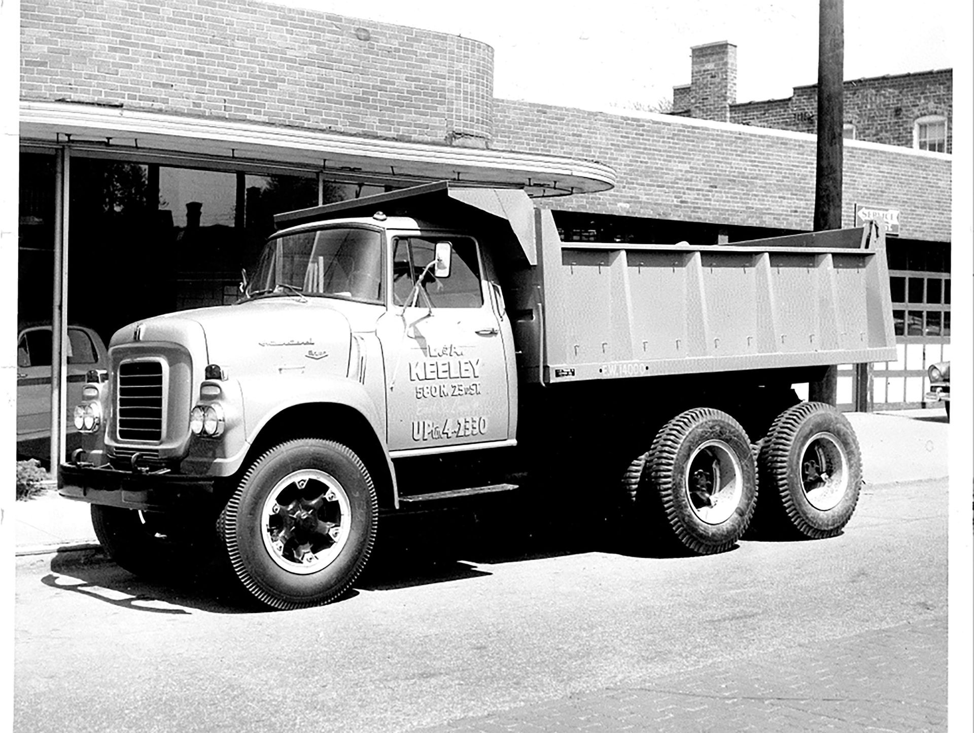 A black and white photo of a dump truck parked in front of a building.