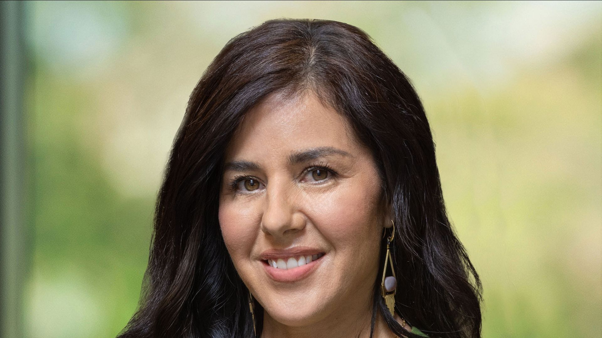 A woman with long dark hair and earrings is smiling for the camera.