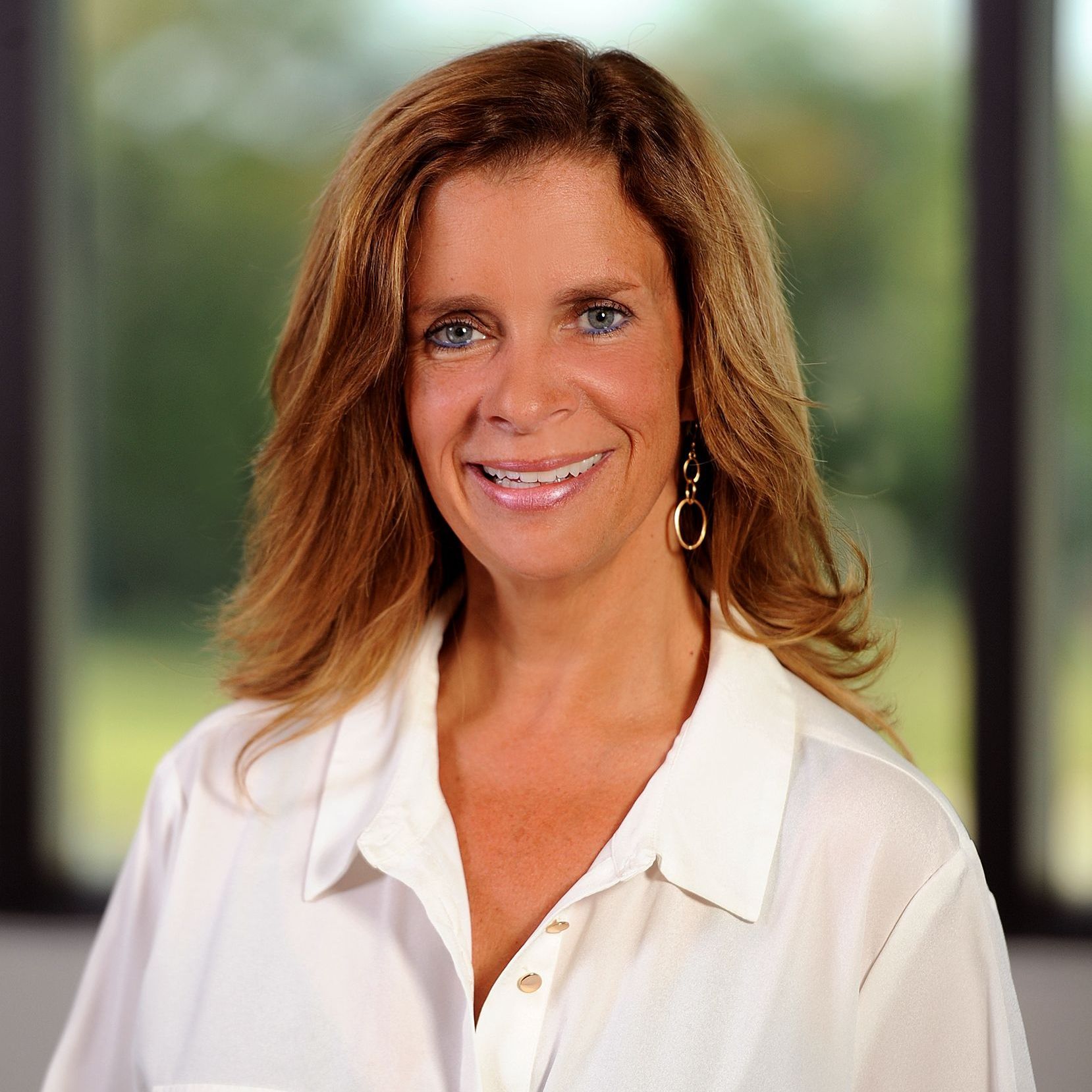 A woman wearing a white shirt and earrings is smiling for the camera.