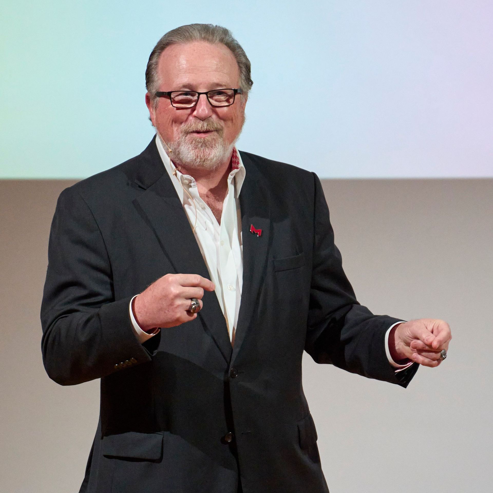 A man in a suit and glasses is giving a presentation