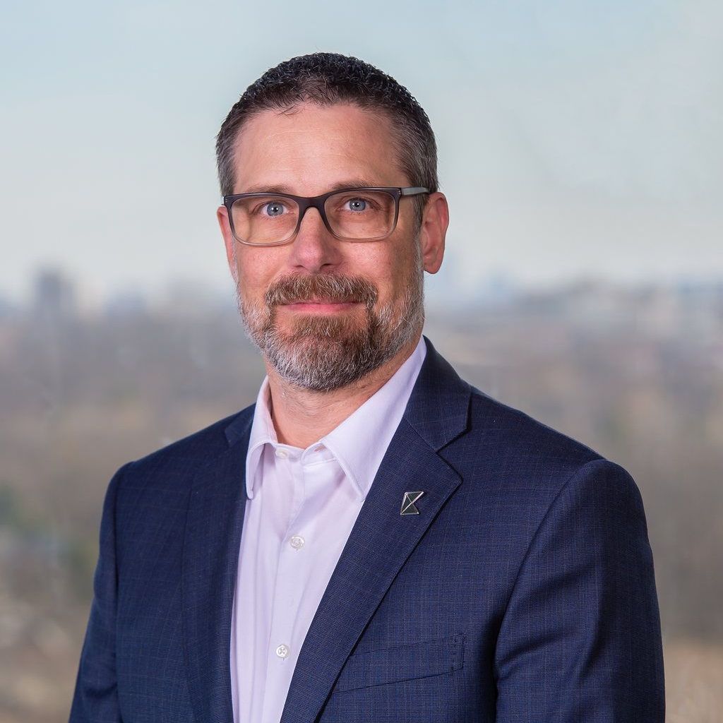 A man with a beard and glasses is wearing a blue suit and white shirt.