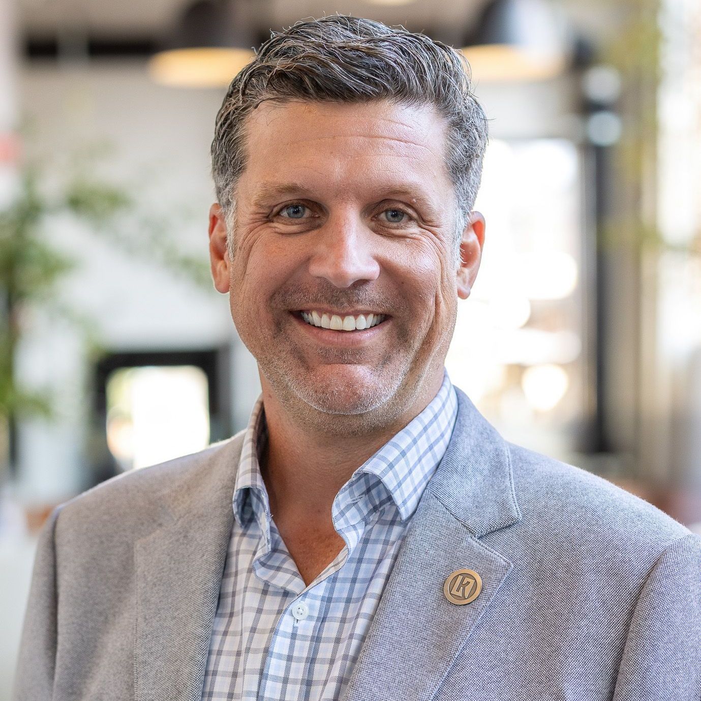 A man in a suit and plaid shirt is smiling for the camera.