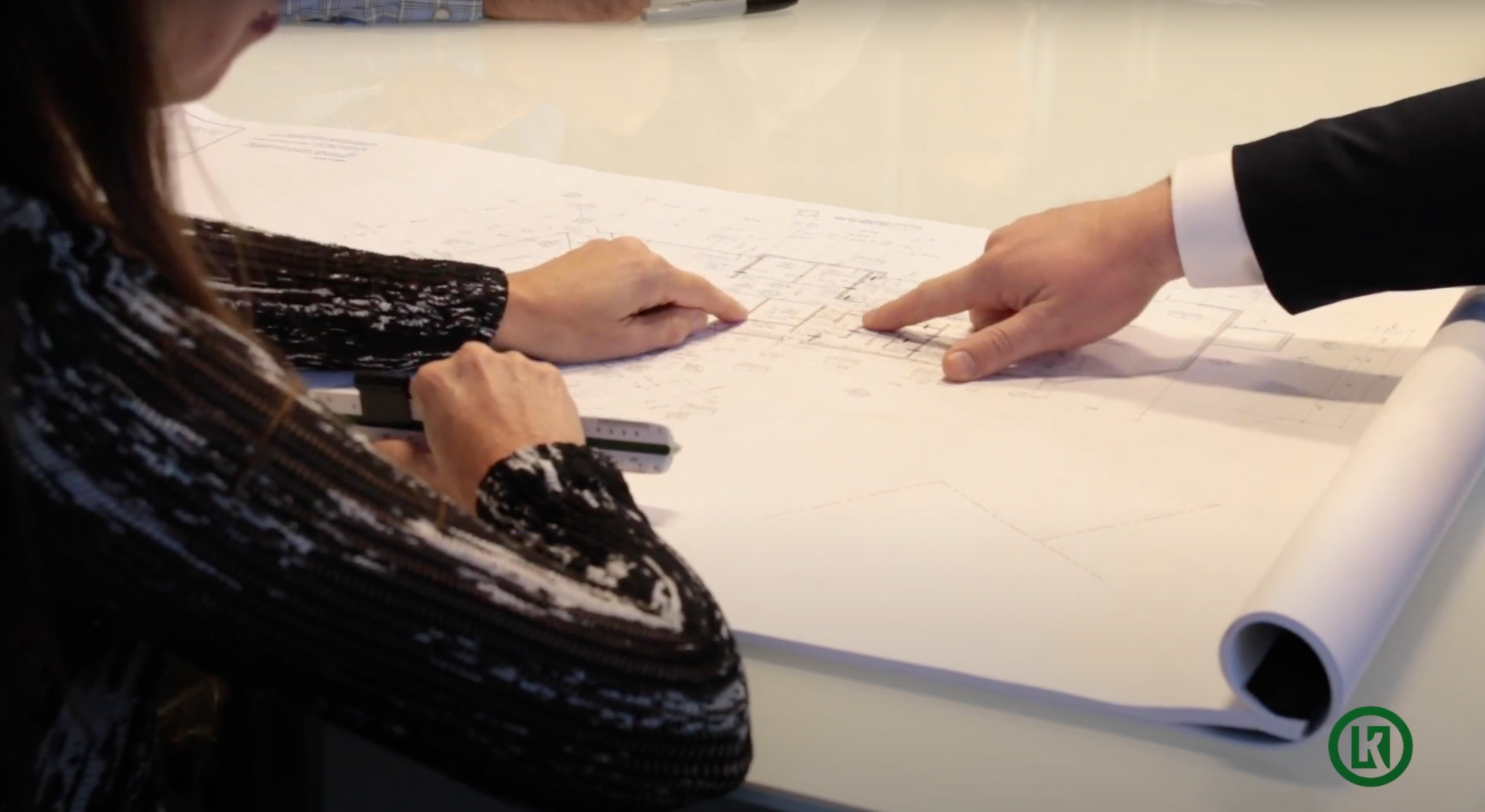 A man and a woman are sitting at a table looking at a blueprint.