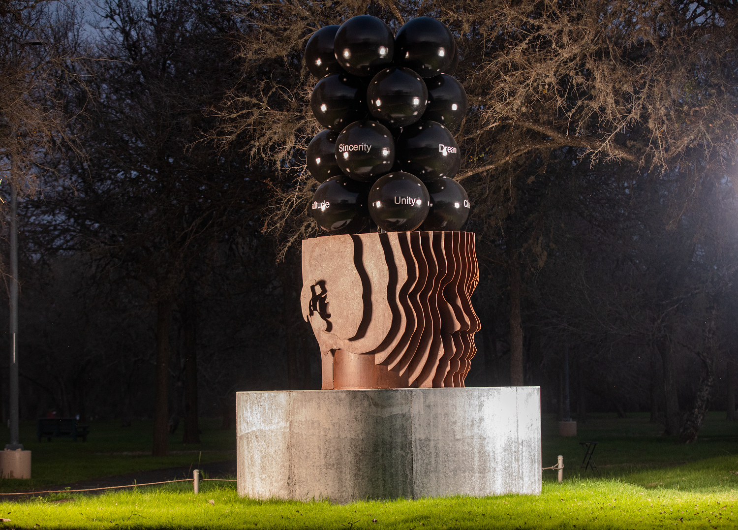 A sculpture of a head with a bunch of black balls on top of it